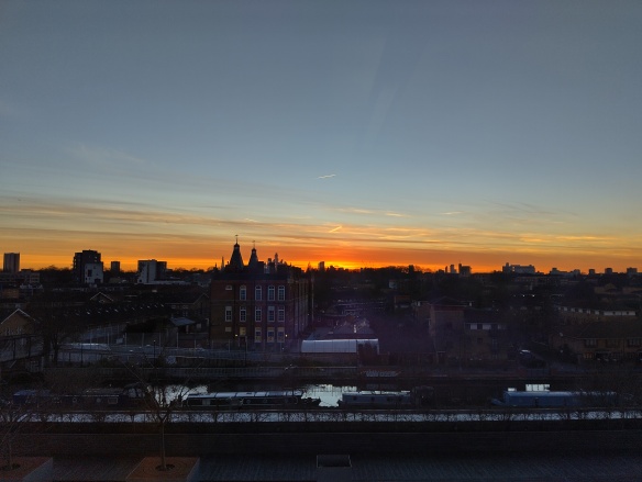 Sunset of orange and blue sky with a skyline of buildings in silhouette